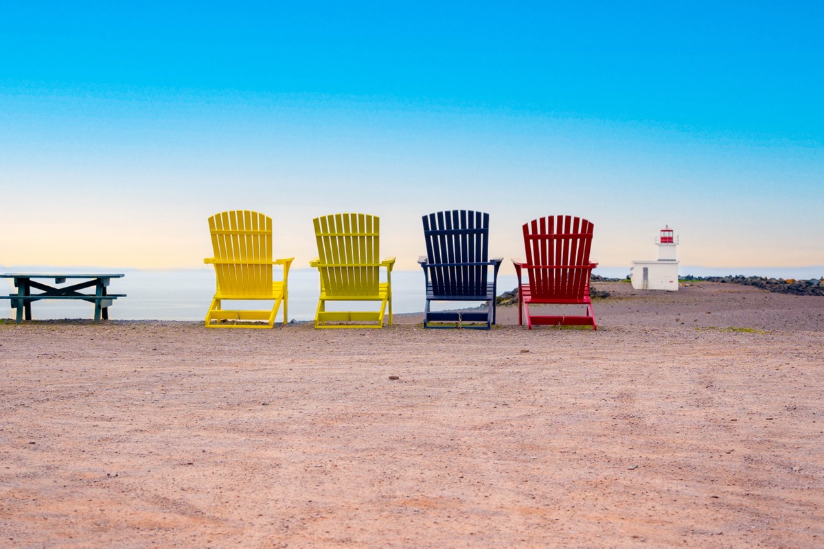 Colourful Adirondack chairs facing the Bay of Fundy with lighthouse in background